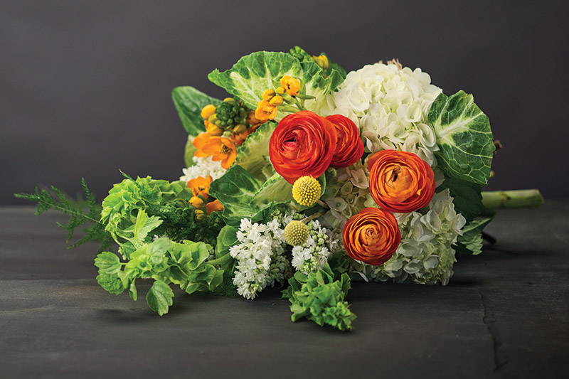 Jen-Mor Florist, Dover, jenmor.com: White ornamental cabbage, star of Bethlehem, orange ranunculus, white French lilac, bells of Ireland, craspedia, asparagus plumosa and white hydrangea.