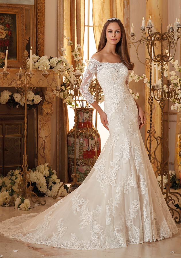 Mori Lee Bridal Style 5477 | Off-the-shoulder wedding dress with three-quarter length illusion sleeves and a scalloped illusion neckline on the sweetheart bodice. Fit-and-flare silhouette is accented with covered buttons and the skirt and chapel train finish in a scalloped lace border hemline. $950, The Dress Matters, Media, Pa., www.thedressmatters.com 